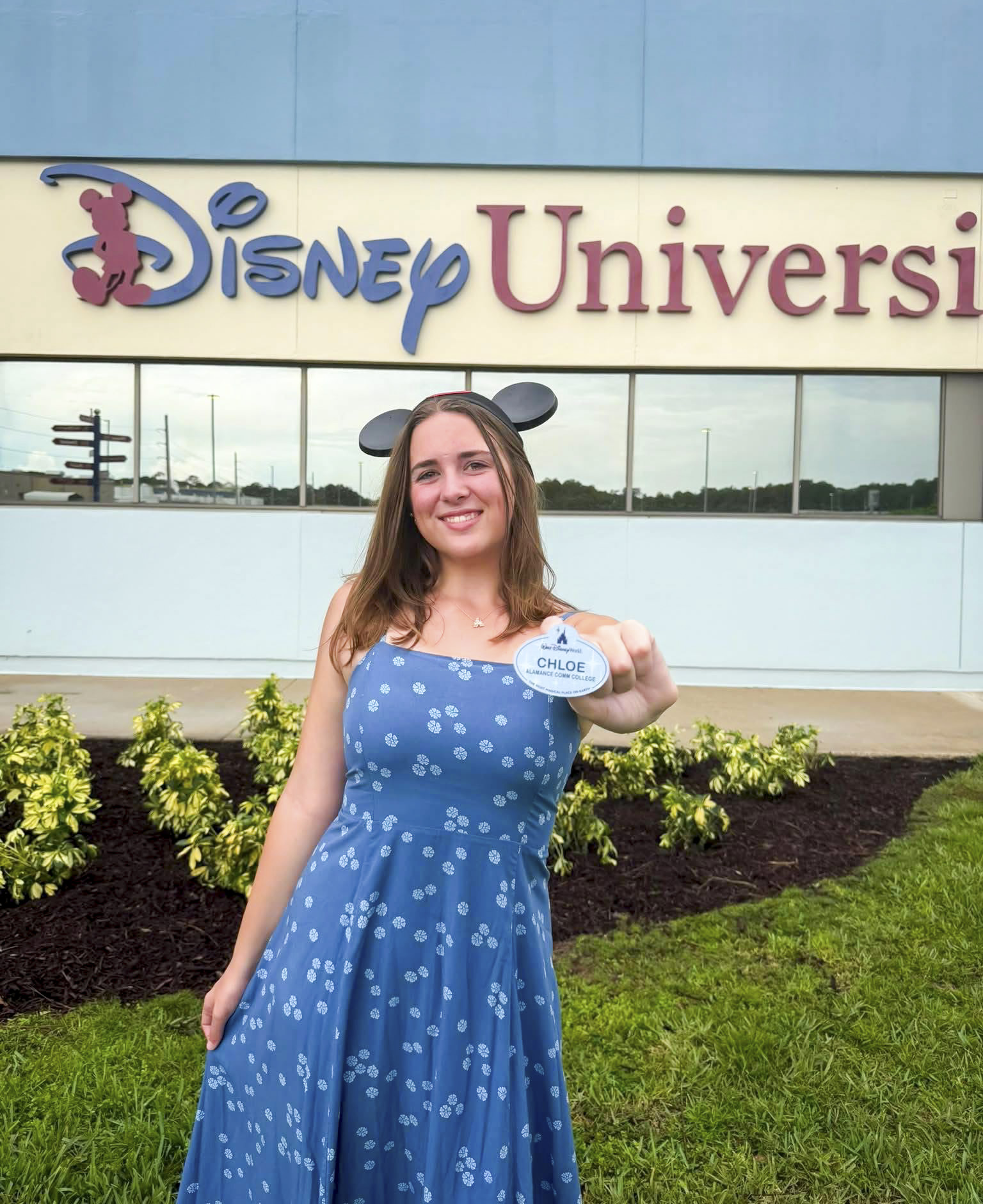 Chloe Williams smiles outside Disney University while holding her Disney College Program name tag, which reads “Chloe — Alamance Community College.”