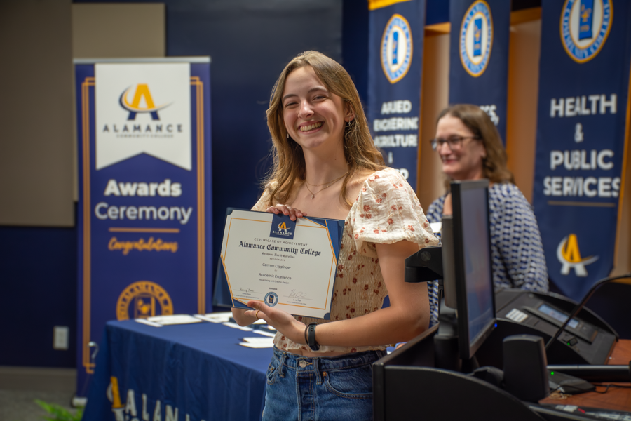 Student smiling while holding a certificate of academic excellence at Alamance Community College’s Awards Ceremony.