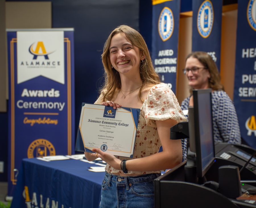 Student smiling while holding a certificate of academic excellence at Alamance Community College’s Awards Ceremony