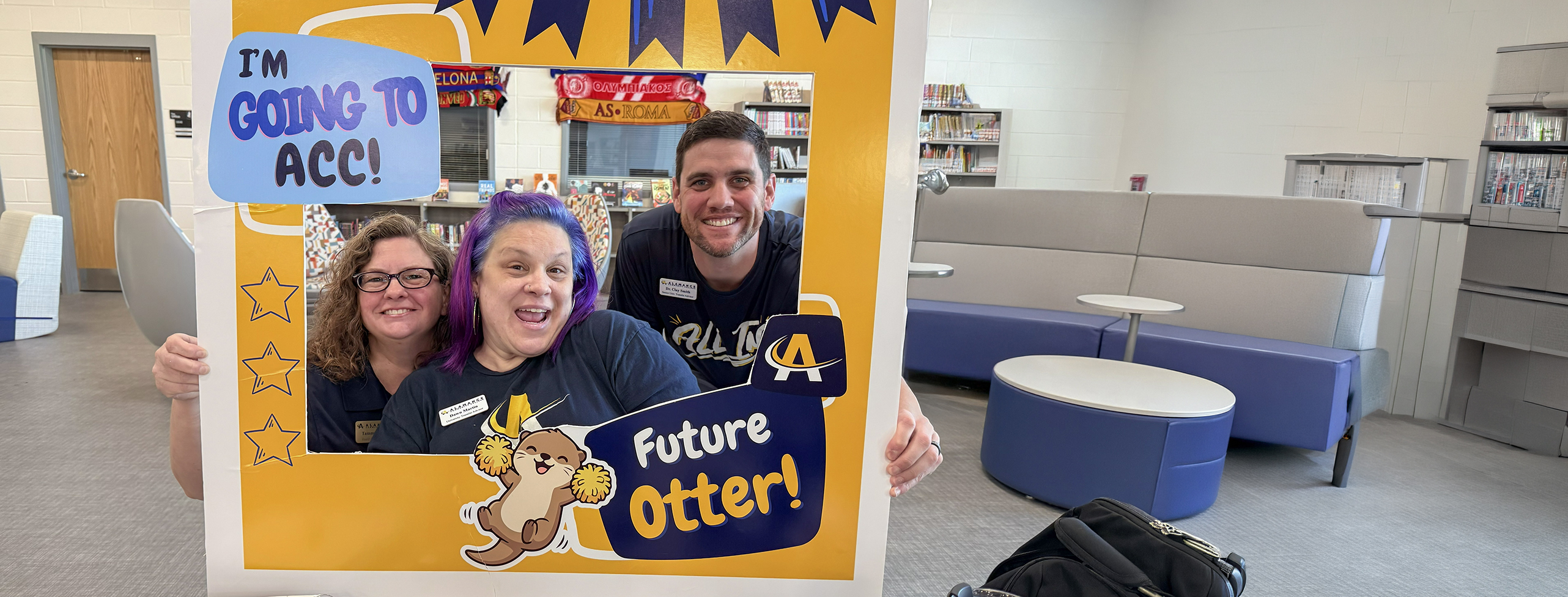 Academic Advising Three staff members smiling and posing behind a photo frame sign that reads 'I’m going to ACC! Future Otter!' inside a campus library space.