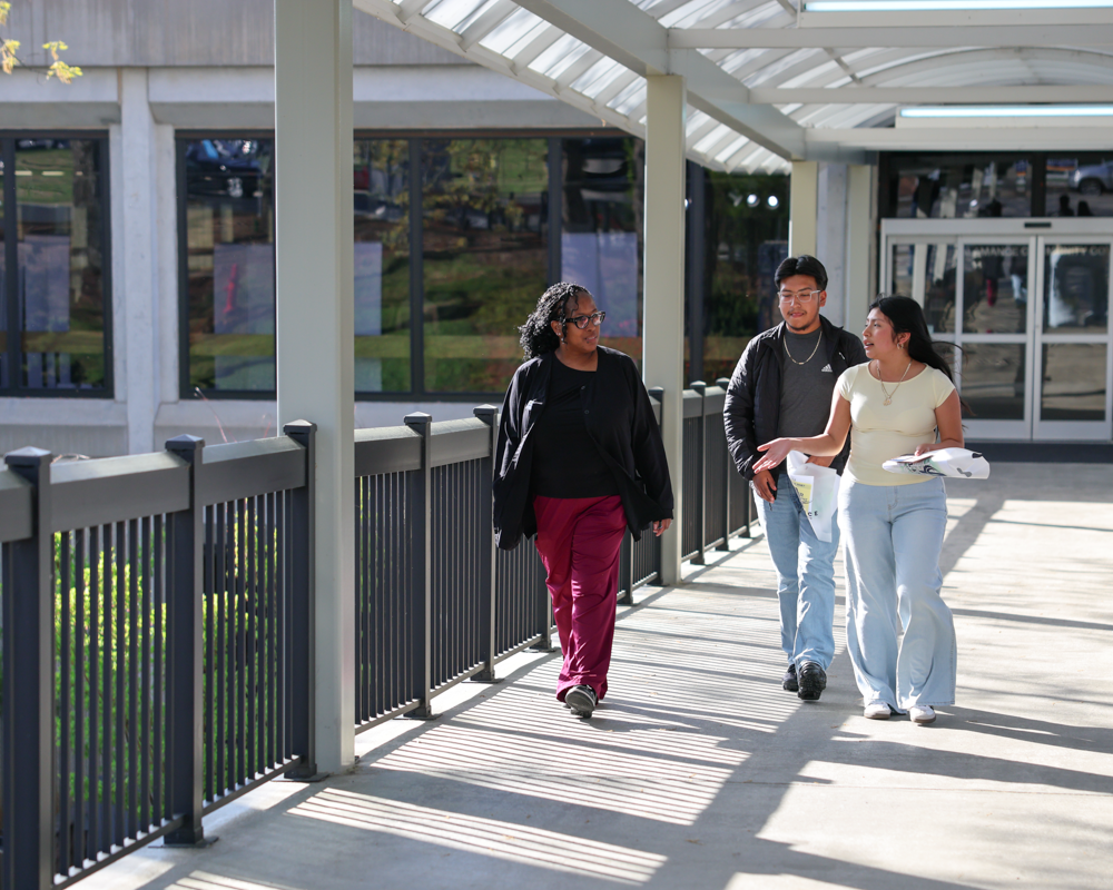 “Three Alamance Community College students walking and talking together along a covered outdoor campus walkway.