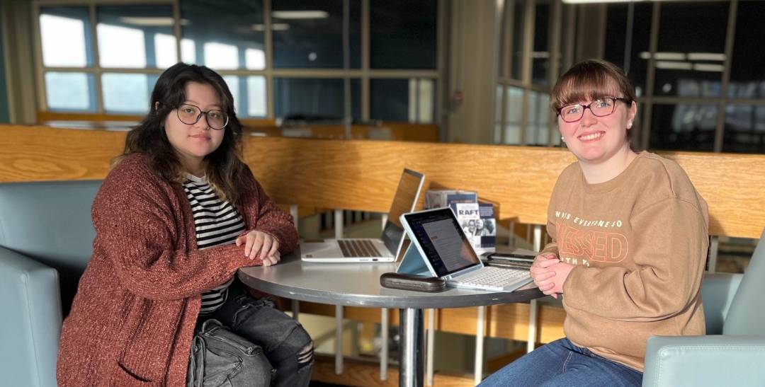 two female acc students sitting at a table smiling at camera