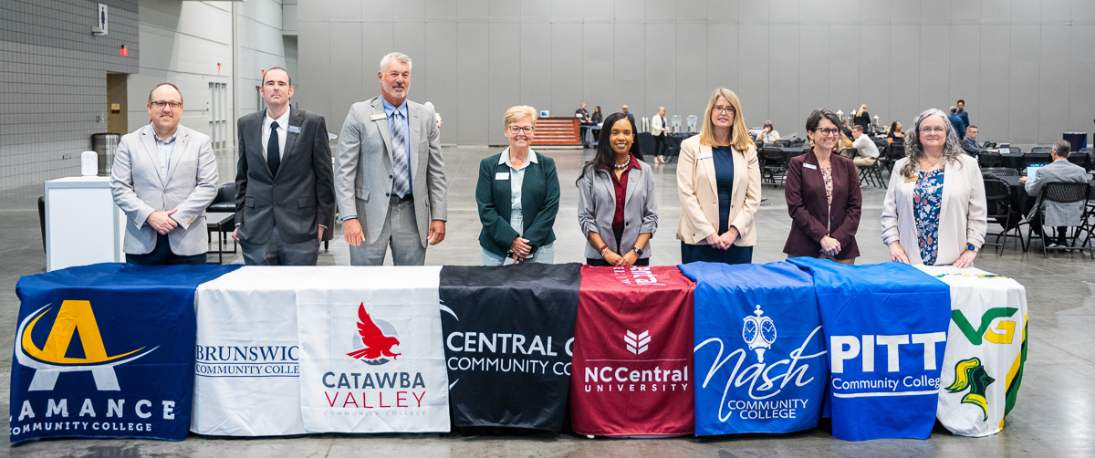 college presidents standing in front of a table with their colleges banners in front of them sitting on a table